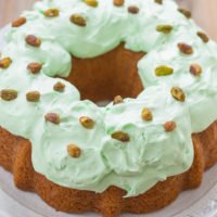 A bundt cake with green icing and pistachio toppings on a plate.