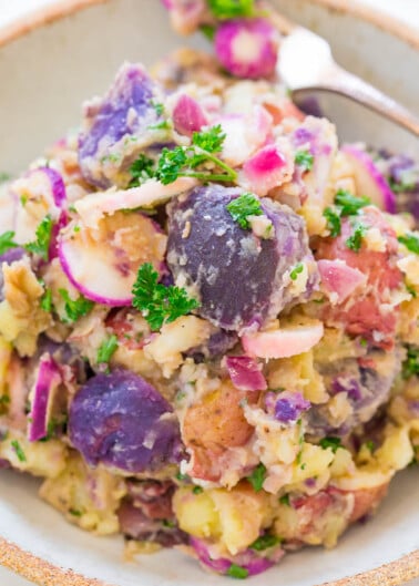 A bowl of colorful potato salad garnished with parsley.