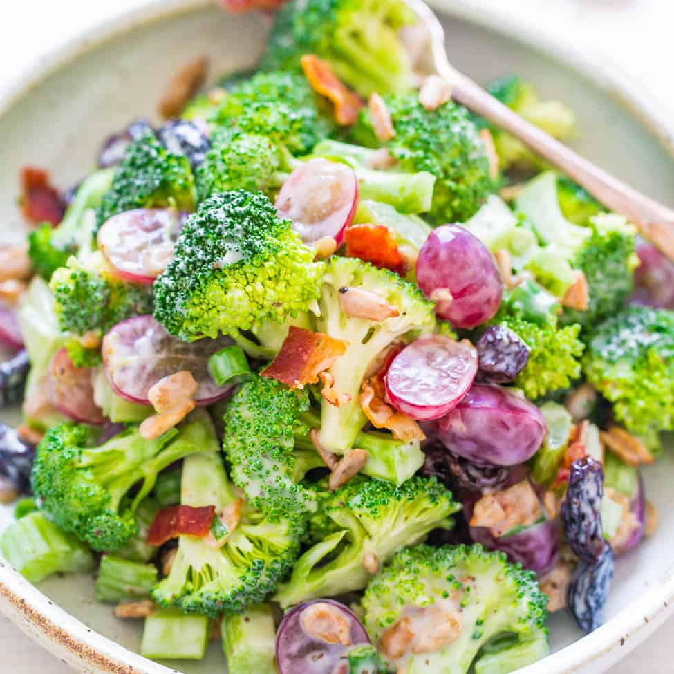 A bowl of broccoli salad with grapes, bacon, and a creamy dressing.