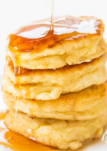 Stack of pancakes with syrup being poured on top.