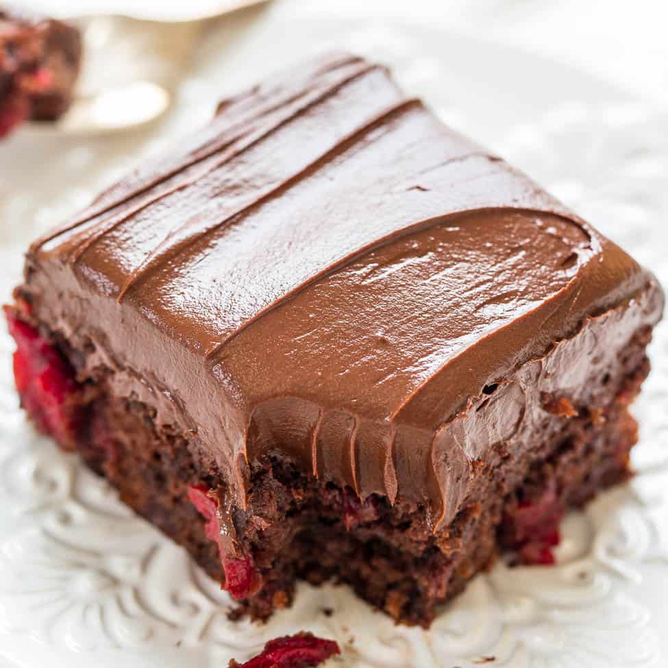 A chocolate frosted brownie with raspberry pieces on a decorative plate.