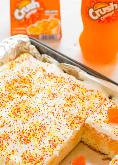 A cake with white frosting and orange sprinkles, accompanied by orange-flavored crush soda.