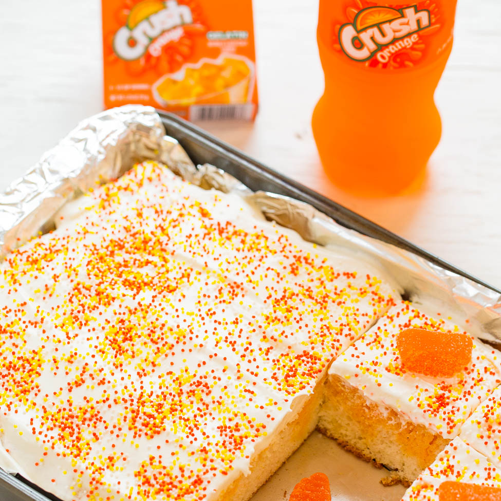 A cake with white frosting and orange sprinkles, accompanied by orange-flavored crush soda.
