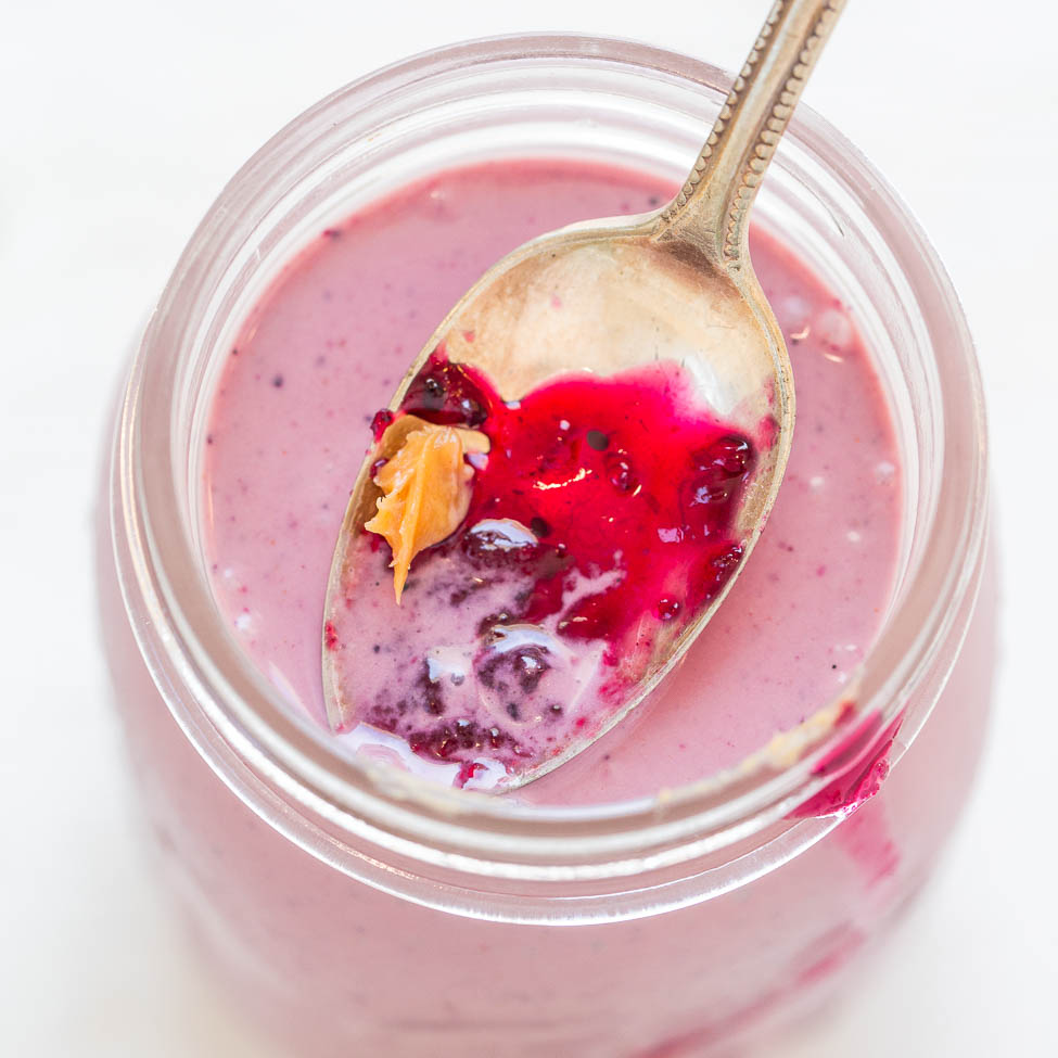 A spoon rests in a jar of mixed berry yogurt with visible fruit pieces.