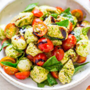 Bowl of pesto pasta salad with cherry tomatoes and fresh basil leaves.
