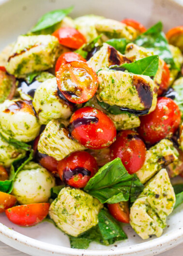 Bowl of pesto pasta salad with cherry tomatoes and fresh basil leaves.