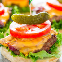 Cheeseburger with a pickle on top, lettuce, tomato, and melted cheese.