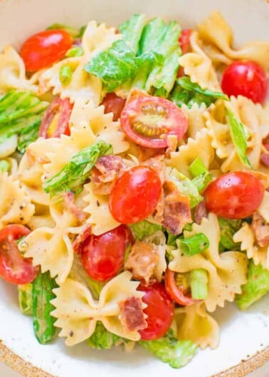 A bowl of bow-tie pasta salad with cherry tomatoes, greens, and bacon bits.