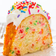 A slice of rainbow sprinkle funfetti cake with white frosting.