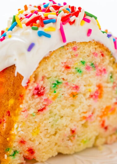 A slice of rainbow sprinkle funfetti cake with white frosting.