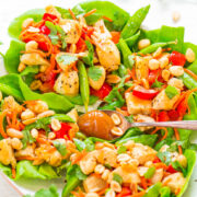 A vibrant chicken salad with snow peas, cherry tomatoes, peanuts, and herbs served on a plate.