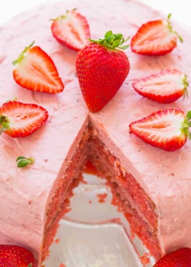 Strawberry cake with a slice removed, showcasing layers and topped with fresh strawberry slices.