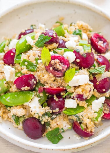 A bowl of quinoa salad with snap peas, grapes, herbs, and crumbled cheese.