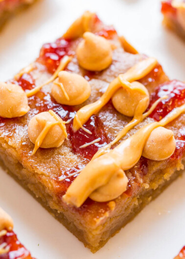 A close-up of a square piece of dessert topped with peanuts and a drizzle of caramel.
