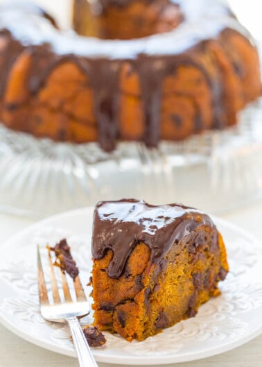 A slice of pumpkin bundt cake with chocolate glaze on a white plate, with the remaining cake in the background.