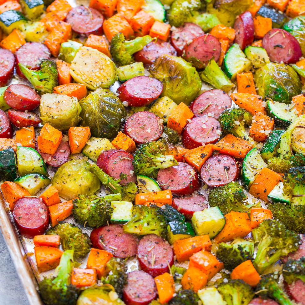 Assorted roasted vegetables and sliced sausage on a baking sheet.