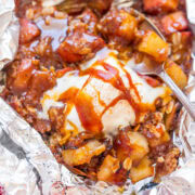 A dish of baked apple dessert topped with caramel sauce, served in aluminum foil.