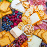 A colorful charcuterie board with an assortment of cheeses, cured meats, crackers, nuts, and fresh fruit.