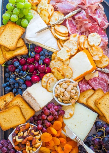 A colorful charcuterie board with an assortment of cheeses, cured meats, crackers, nuts, and fresh fruit.