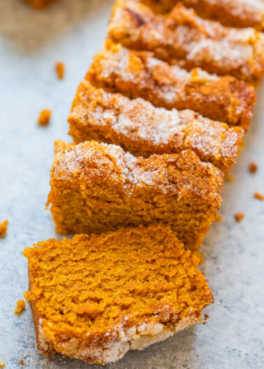 Sliced pumpkin bread with a sugary crust on a baking sheet.