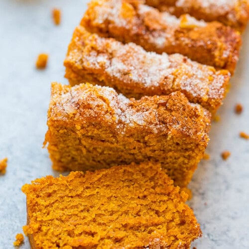 Sliced pumpkin bread with a sugary crust on a baking sheet.