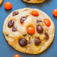 Freshly baked chocolate chip cookies with orange-colored candies on a dark surface.
