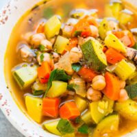 A bowl of colorful vegetable soup with beans, carrots, zucchini, and herbs.