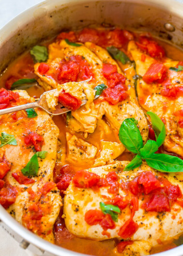 A pot containing chicken breasts topped with tomato sauce and garnished with basil leaves.