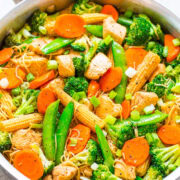 A colorful stir-fry with chicken, broccoli, carrots, snap peas, and corn in a pan.