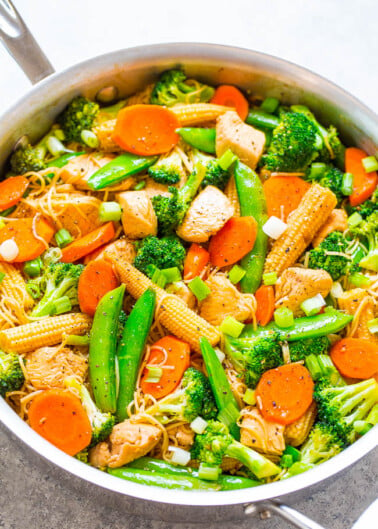 A colorful stir-fry with chicken, broccoli, carrots, snap peas, and corn in a pan.