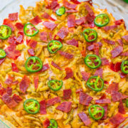 A layered dip topped with crispy bacon and jalapeño slices, served with crackers.