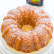 Glazed lemon bundt cake on a plate with a lemon extract bottle in the background.