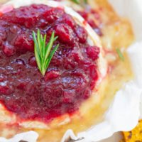 Baked brie with a cranberry topping garnished with a sprig of rosemary.