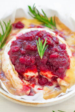 Baked brie cheese topped with cranberry sauce and garnished with rosemary sprigs.