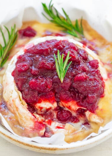 Baked brie cheese topped with cranberry sauce and garnished with rosemary sprigs.