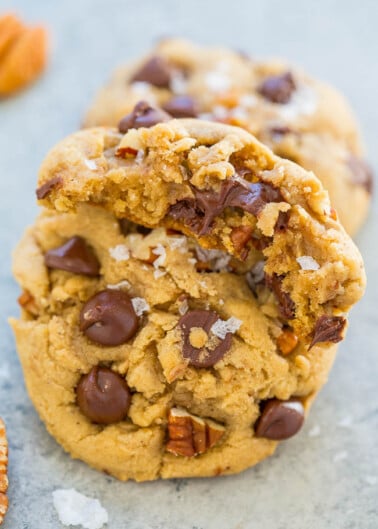 A freshly baked chocolate chip cookie with pecans, showing a textured surface with visible chocolate chips and a bite taken out of it.