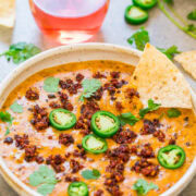A bowl of spicy chili garnished with jalapeño slices and cilantro, served with tortilla chips and a glass of rosé wine.