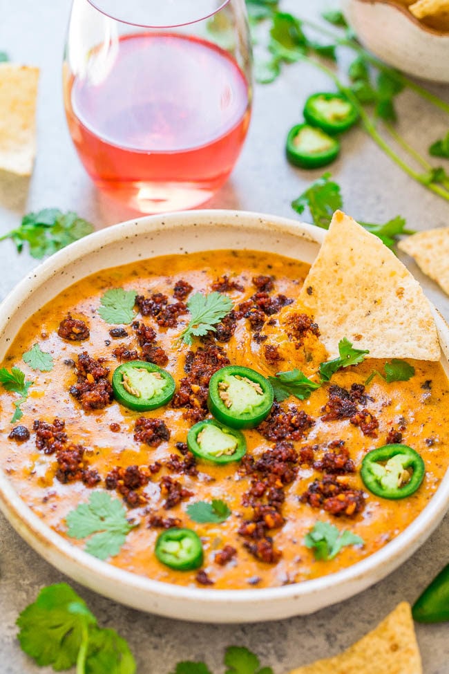 A white bowl of Spicy Chorizo Queso with a glass of wine