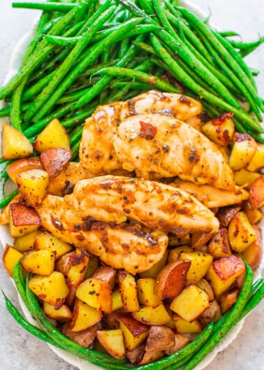 A plate of grilled chicken breasts with a side of roasted potatoes and green beans.