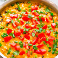 A pot of colorful chili garnished with diced tomatoes, green onions, and cilantro.