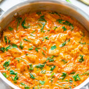 A skillet with creamy tomato spinach pasta sauce, garnished with fresh herbs.