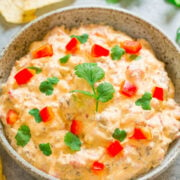 A bowl of creamy dip garnished with red bell pepper and cilantro, accompanied by crackers.