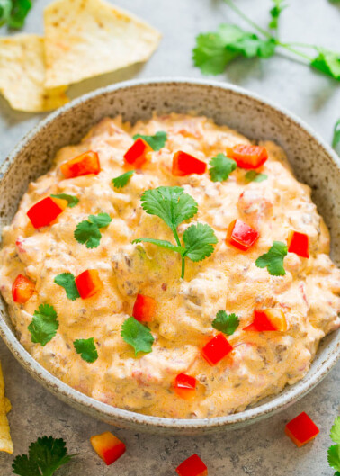 A bowl of creamy dip garnished with red bell pepper and cilantro, accompanied by crackers.