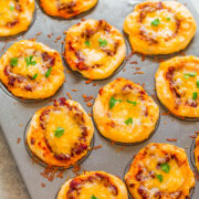 Mini cheese-topped pizzas on a baking sheet with some garnished with herbs.