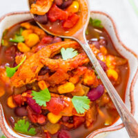 A vibrant bowl of vegetable chili garnished with fresh cilantro, served with a spoonful above it.