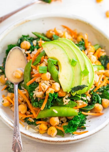 A bowl of salad with chickpeas, avocado, greens, shredded carrots, and a creamy dressing.