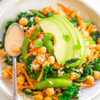 A bowl of kale and chickpea salad topped with sliced avocado and a creamy dressing.