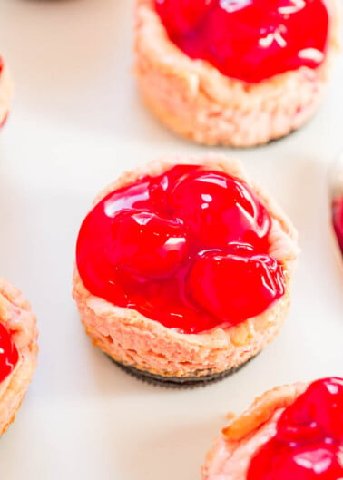 Mini cherry cheesecakes on a white surface.