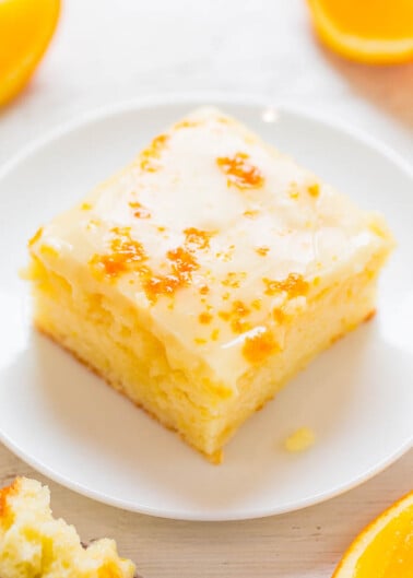 A slice of citrus-glazed cake on a white plate, with orange slices in the background.