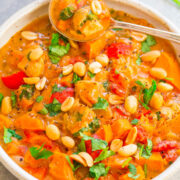 A bowl of hearty vegetable stew with chickpeas, tomatoes, and carrots, garnished with fresh herbs and peanuts.
